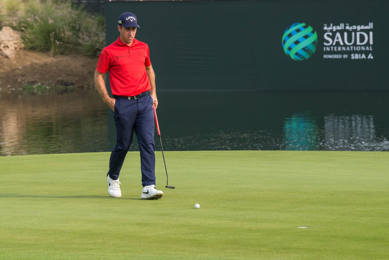 A male golfer in red shirt on a golf course at Saudi International event.